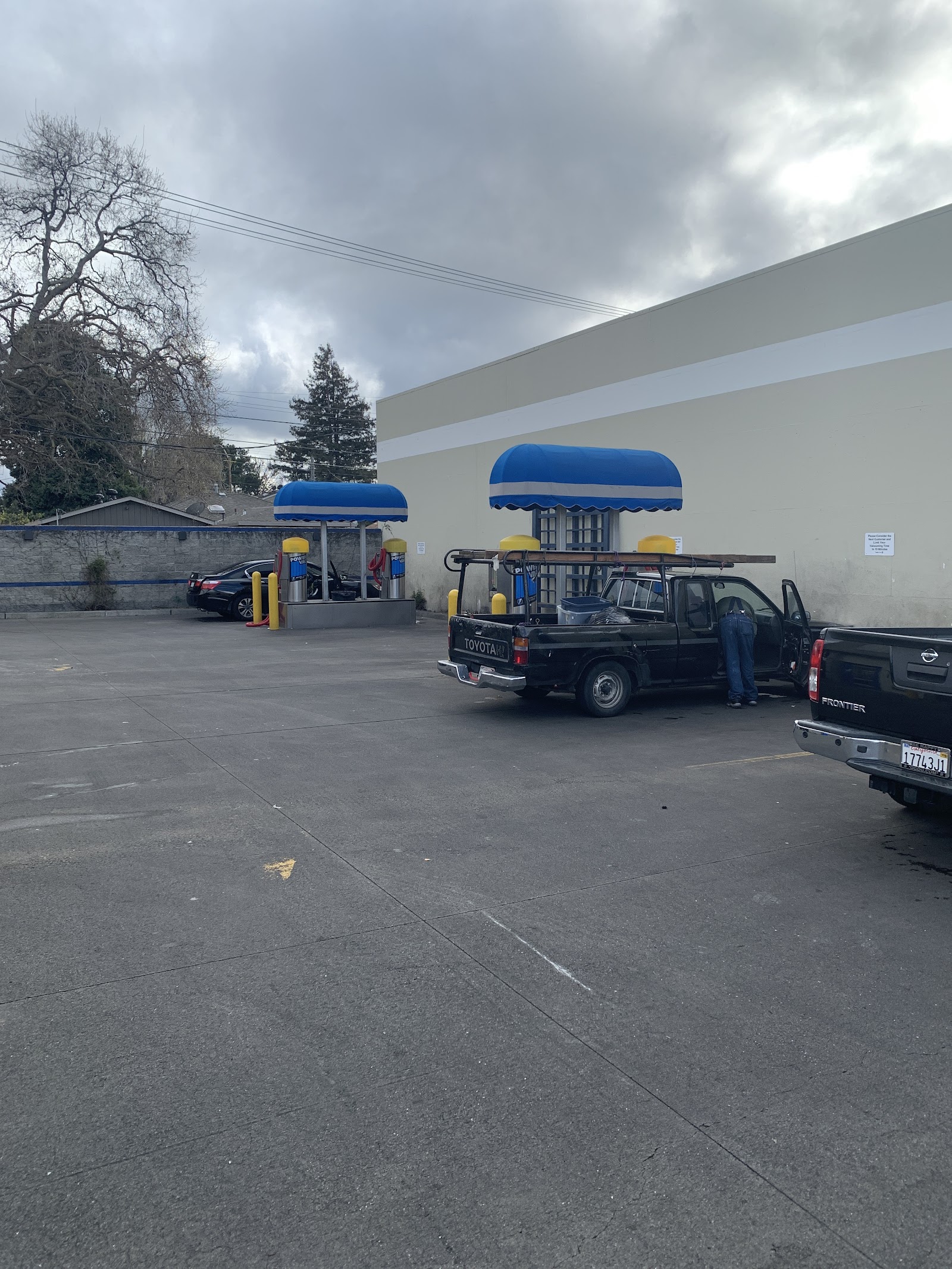 Two blue-dome vacuum awnings at Clear Water Car Wash with yellow bollards beside a work truck